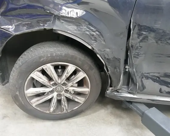 Beschädigter Kotflügel und zerkratztes Rad eines schwarzen Autos nach einem Unfall.