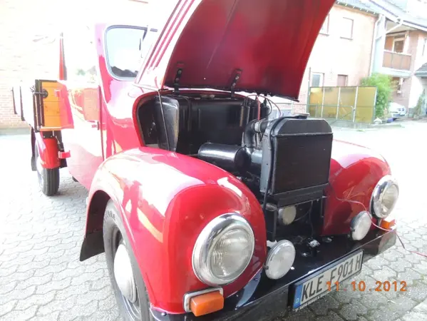 Roter Oldtimer-Lkw mit offener Motorhaube, sichtbar auf einem gepflasterten Hof.