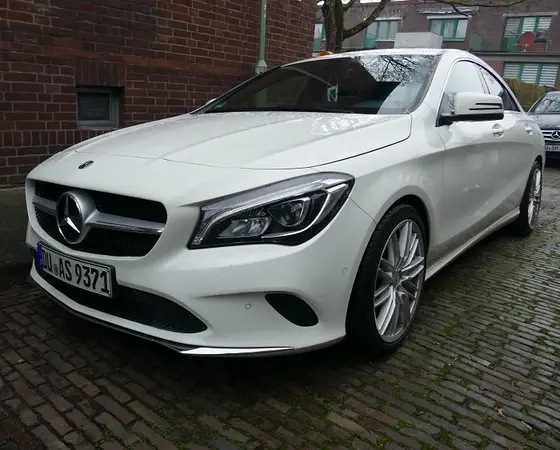 Weißer Mercedes-Benz CLA parkt auf Kopfsteinpflaster vor Backsteinwand in urbaner Umgebung.